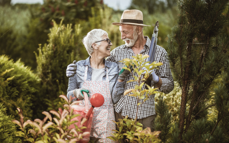 Senior couple look at each other fondly while standing in their garden.