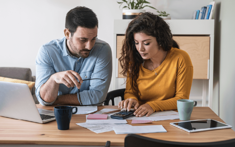 A focused married couple manage finances, use internet banking service on computer and calculator at desk