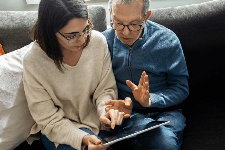 Daughter sitting on sofa with elderly father looking at an iPad.